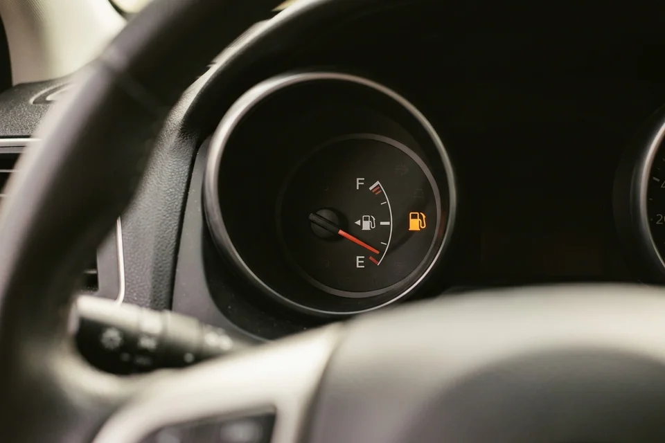 Fuel gauge needle resting on empty with the low fuel warning lit, seen from the driver's seat of a stopped car