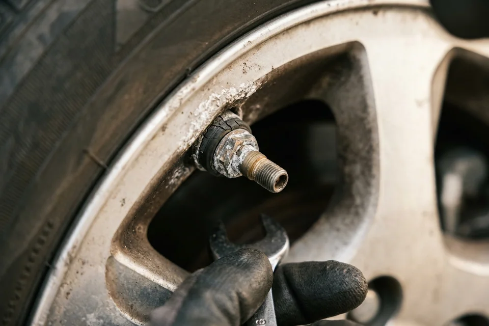 Close view of a metal TPMS valve stem with white corrosion around the nut where it meets the alloy wheel